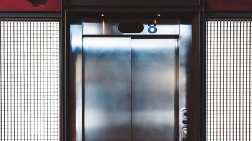 Grungy indoor elevator with chrome doors and metal backlit grid on the sides; modern lift entrance with inscriptions "eight" on the top