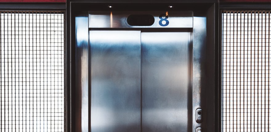 Grungy indoor elevator with chrome doors and metal backlit grid on the sides; modern lift entrance with inscriptions "eight" on the top