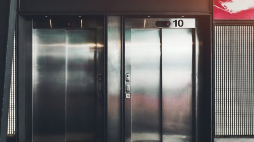 Two contemporary elevator with chrome doors on the street with a huge lamp and inclined roof above; two modern lift entrances with inscriptions "nine" and "ten" on the top on their last floor