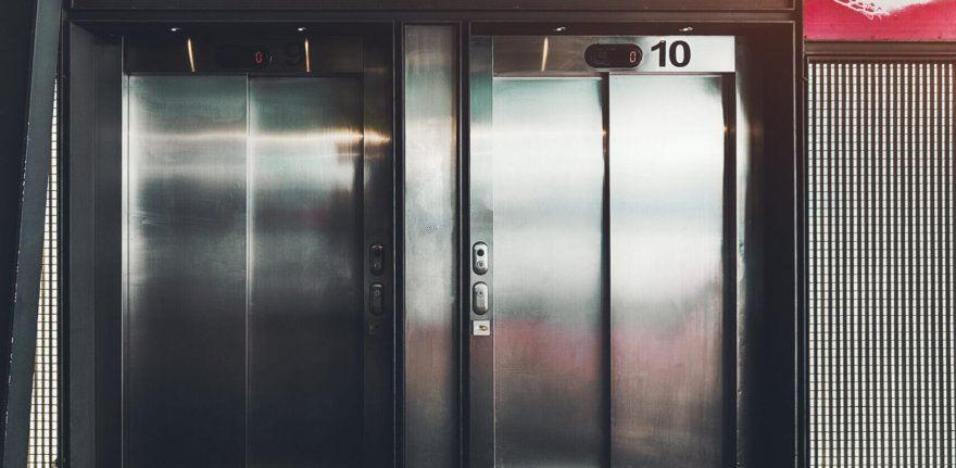 Two contemporary elevator with chrome doors on the street with a huge lamp and inclined roof above; two modern lift entrances with inscriptions "nine" and "ten" on the top on their last floor